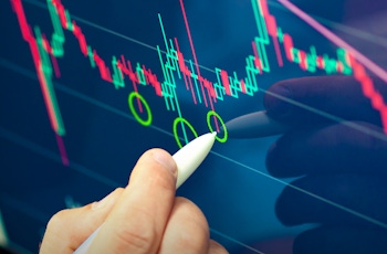 A person's hand holds a stylus, marking points on a colorful financial chart displaying candlestick patterns and trends