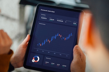 A person holds a tablet displaying a financial account overview with interactive graphs and performance metrics