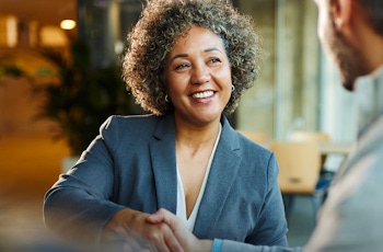 A professional meeting taking place in a modern office, with two individuals shaking hands while seated at a table