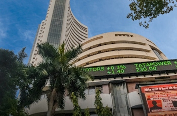 View of the iconic Bombay Stock Exchange (BSE) building in Mumbai, featuring its curved architecture, digital stock ticker with live updates on Tata Motors, Tata Power, Tata Steel, and LT, set against palm trees and urban surroundings