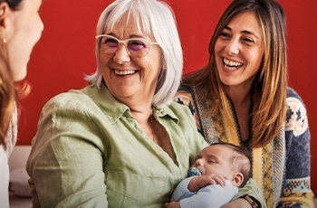 A group of three women gathered, one holding a baby, against a vibrant red wall, conveying warmth and connection