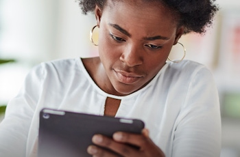 A person in a white blouse holds a tablet, with a bright, modern workspace in the background filled with color swatches