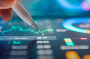 A close-up of a hand holding a stylus, tracing over digital financial charts and graphs on a tablet screen