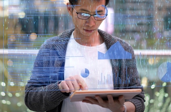 A person interacts with a tablet displaying digital graphs and data analytics in a modern outdoor setting with blurred background lights