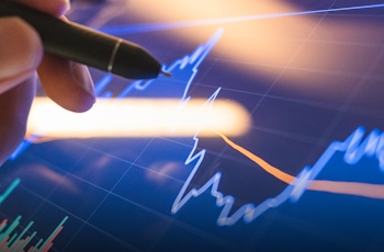Close-up of a hand with a pen pointing at a digital screen displaying dynamic financial charts and market trends, illustrating stock performance and investment analysis.