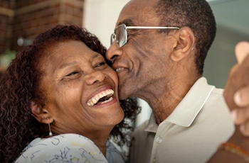 An elderly couple dances closely together, sharing a joyful moment with hands intertwined, set against a cozy interior background