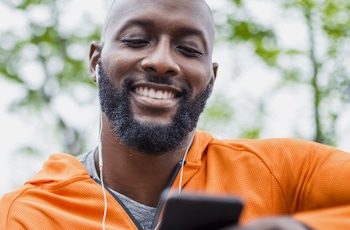 A person in an orange hoodie watches a vodcast on his smartphone, surrounded by a lush green background