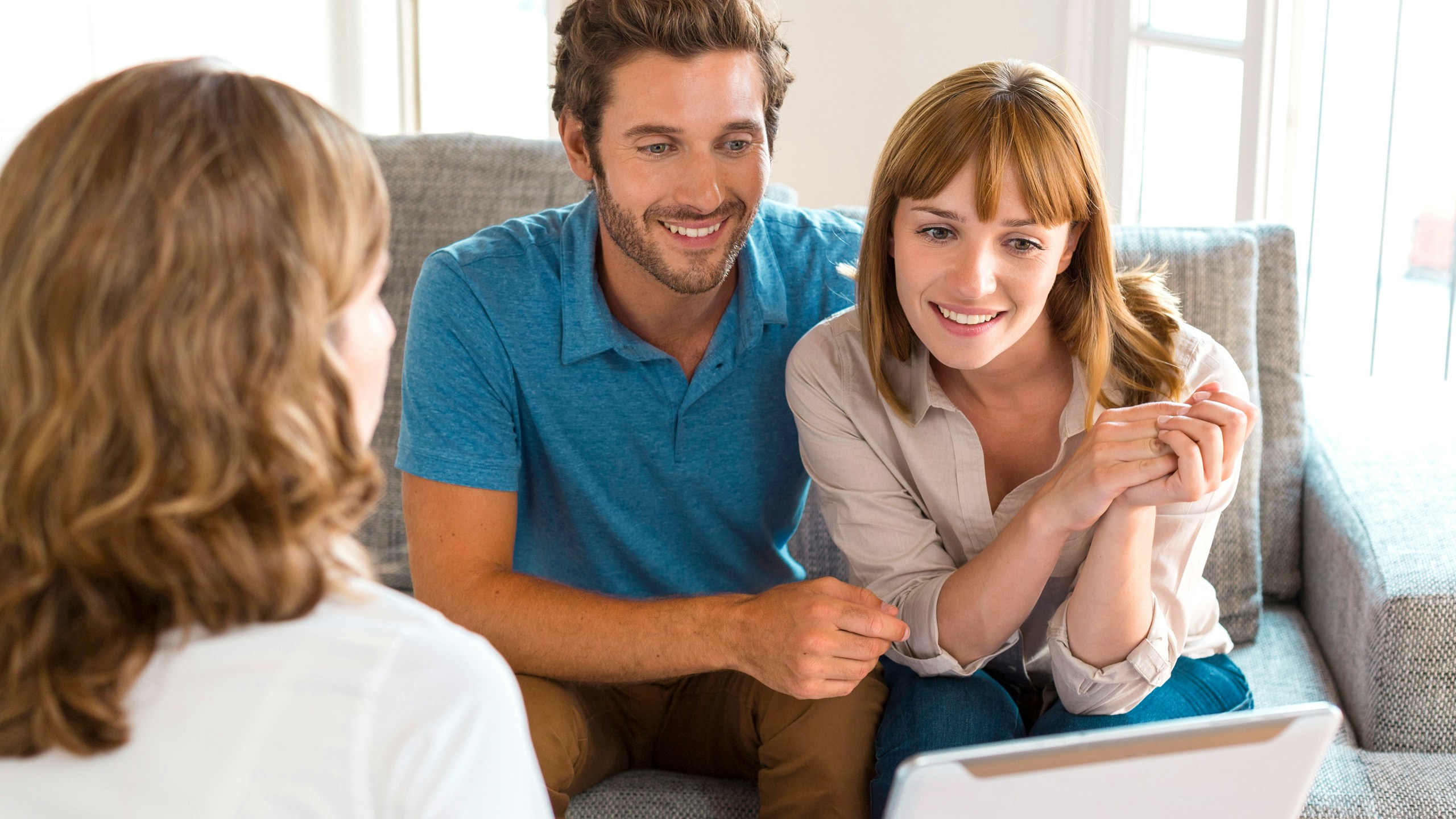 Young couple with adviser looking at tablet in bright livingroom