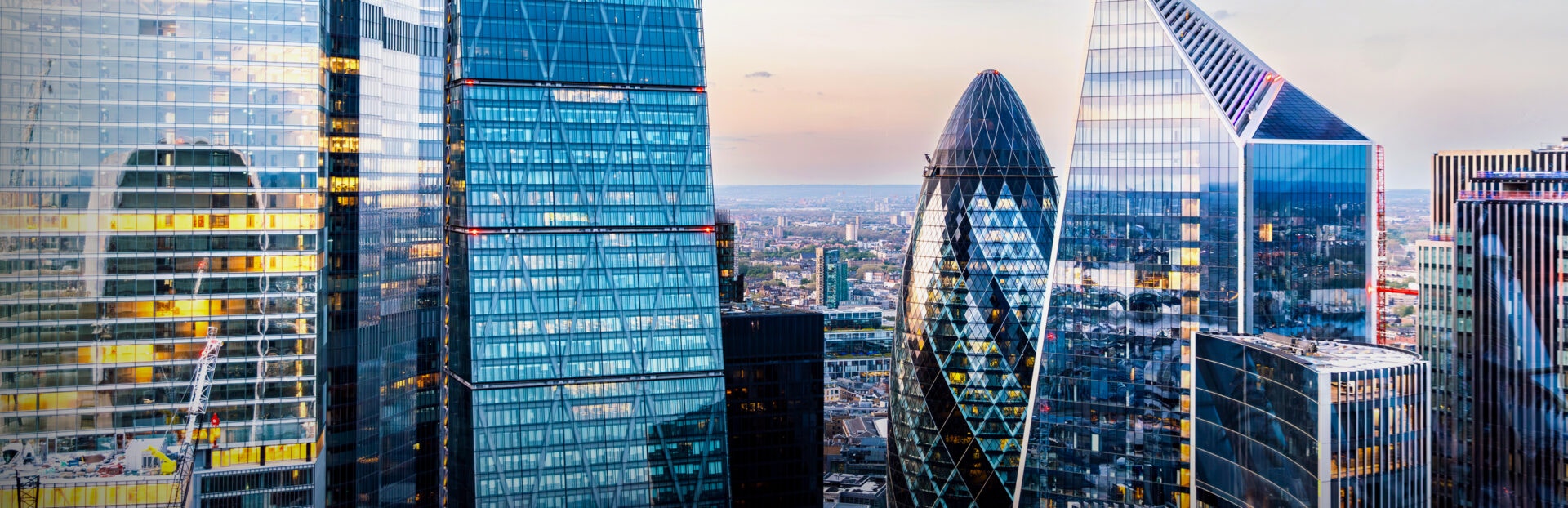 A skyline of modern glass skyscrapers including the iconic "Gherkin" building, reflecting a colorful sunset over the city