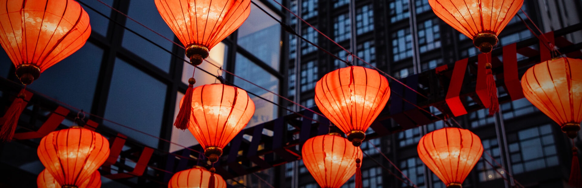 A vibrant display of red lanterns hanging above, against a backdrop of dark glass buildings, creating a festive atmosphere