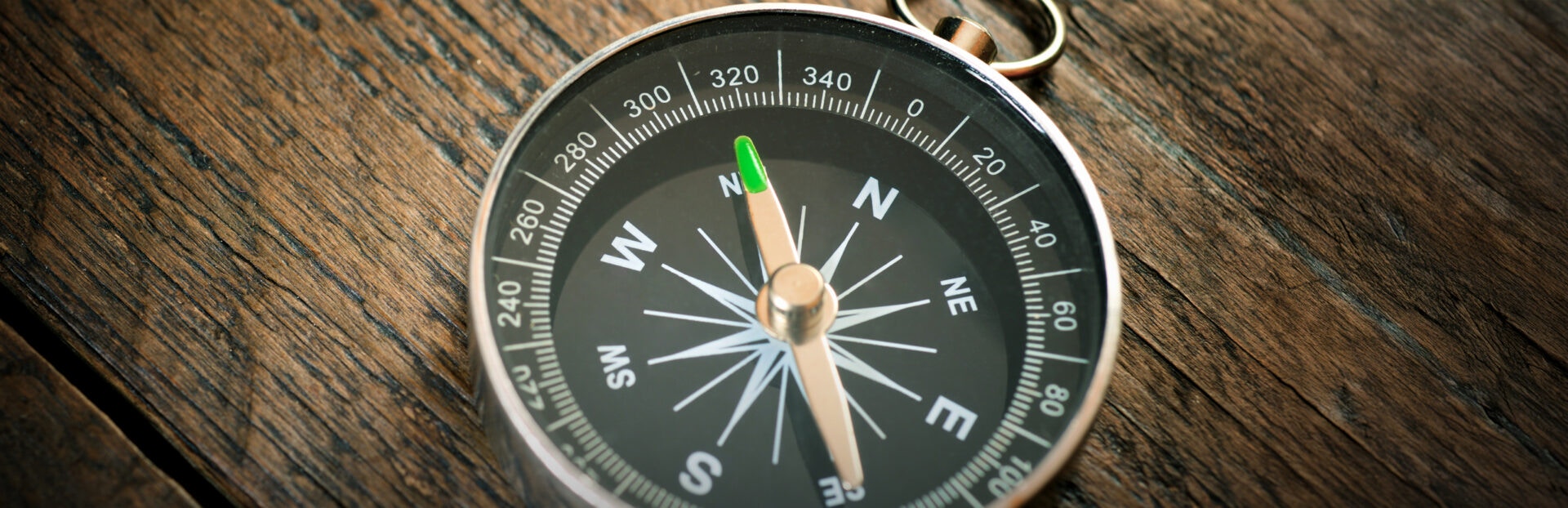 A close-up of a compass resting on a wooden surface, with the needle pointing north, revealing detailed markings and a shiny metal casing.