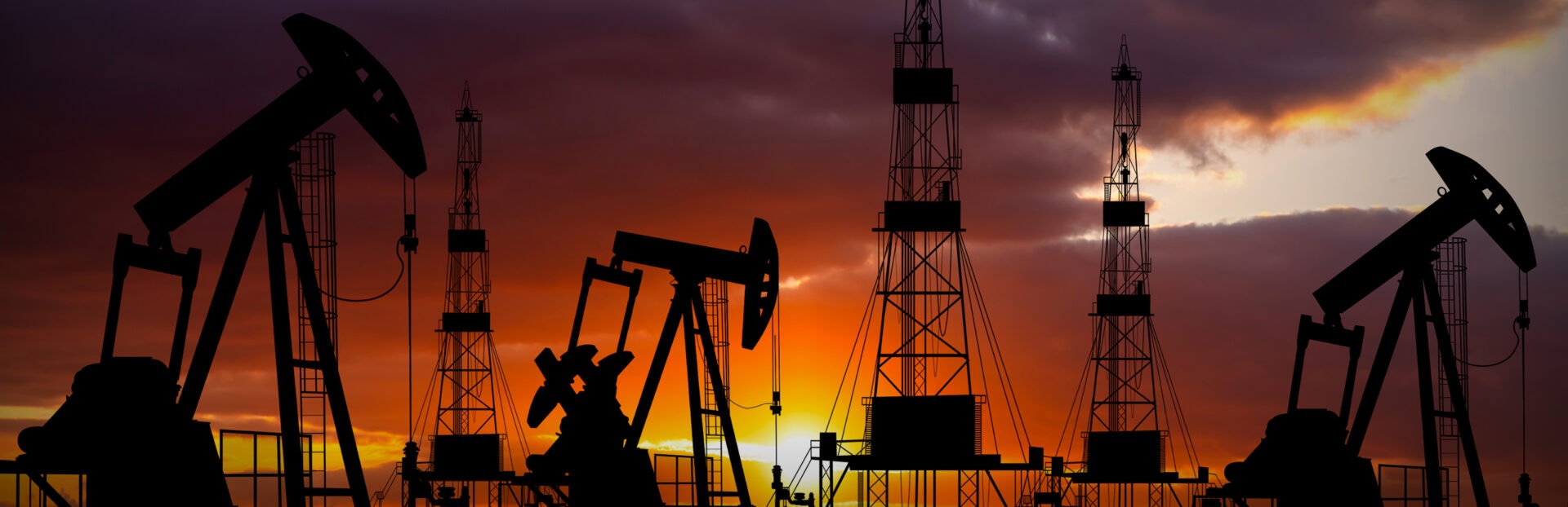 Silhouettes of oil pumps and rigs against a dramatic sunset sky, highlighting the energy industry at dusk