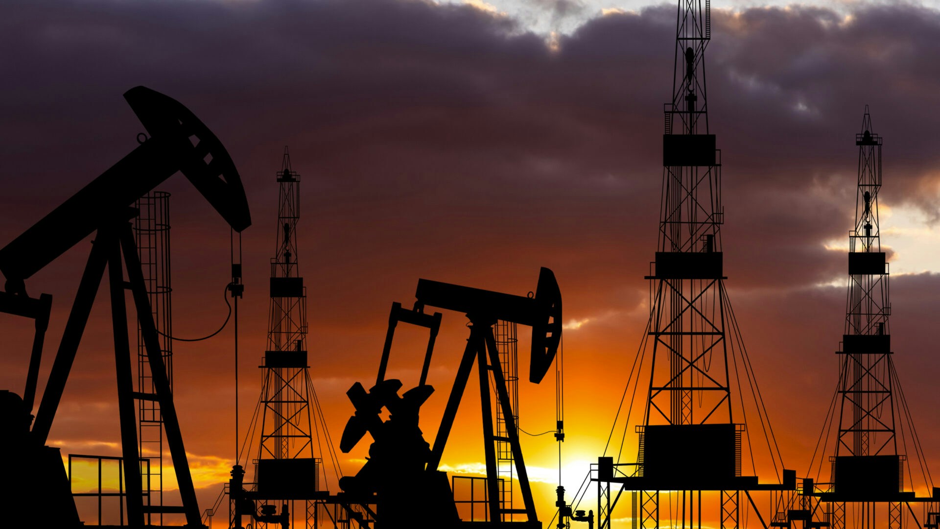 Silhouettes of oil pumps and rigs against a dramatic sunset sky, highlighting the energy industry at dusk