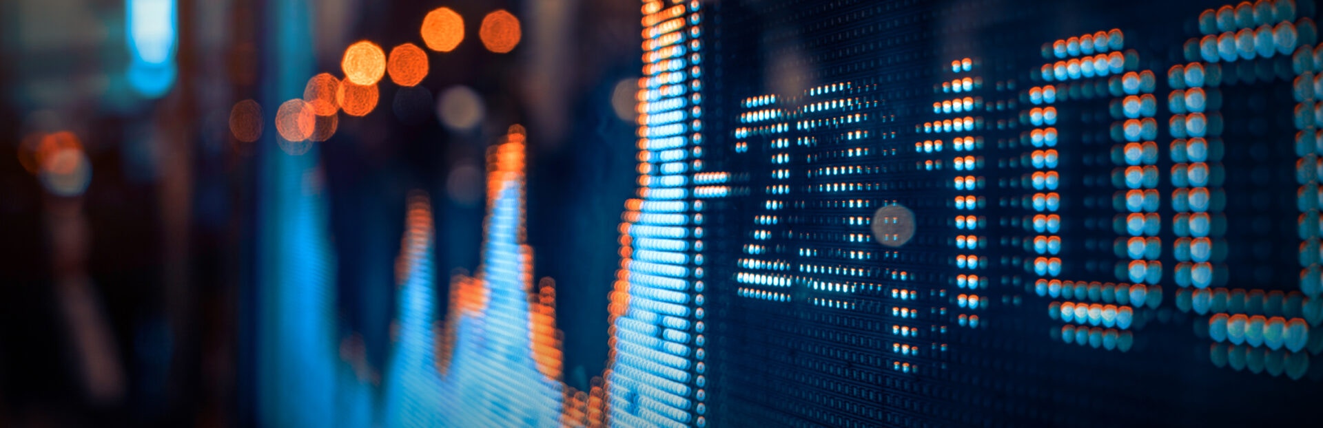 A close-up of a dynamic LED display showing fluctuating stock market statistics, illuminated with vibrant blue and orange lights
