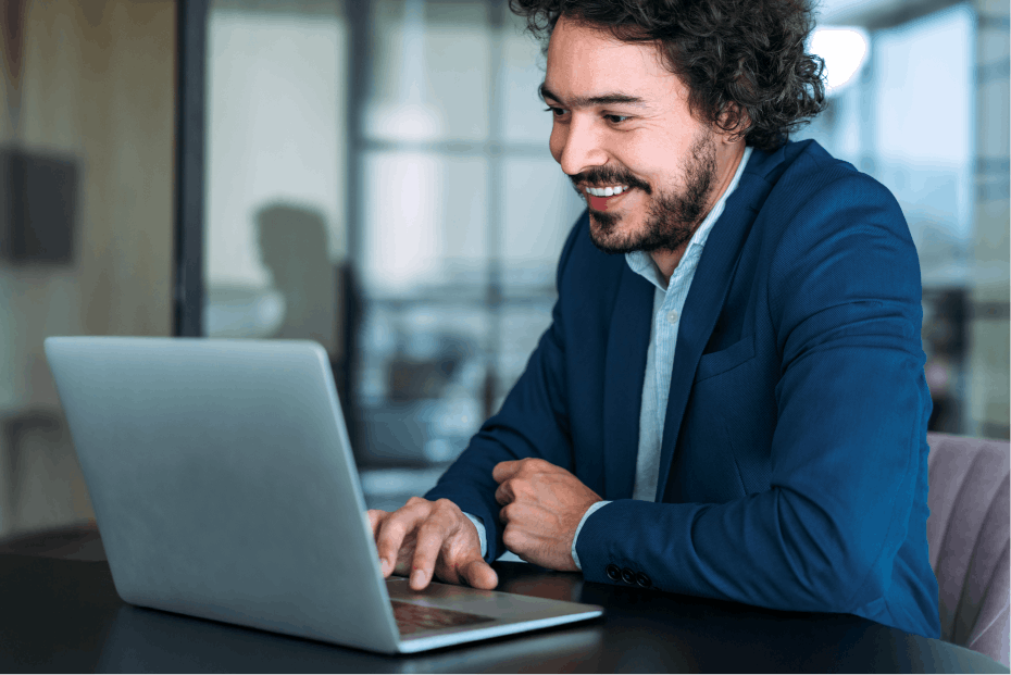 build-your-own-section A man in a blue suit sits at a table, focused on a laptop, with modern office decor in the background