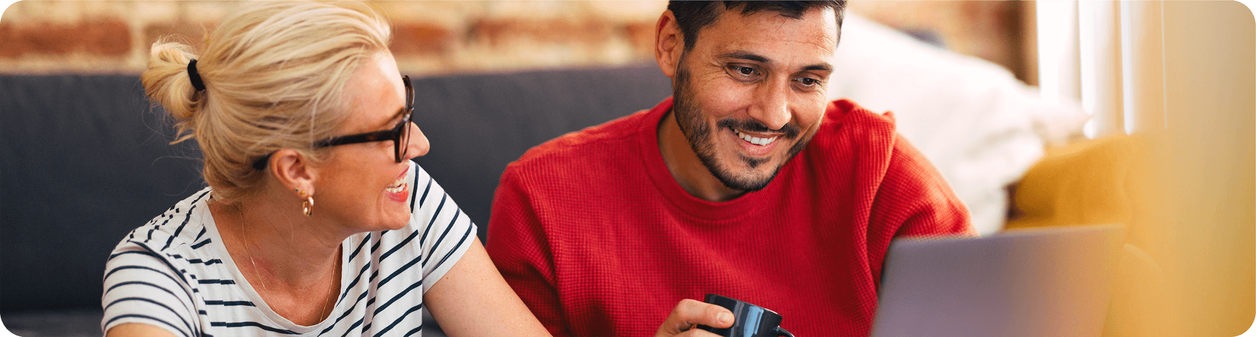 whats-new-generic Two individuals engaged in conversation, one wearing a striped shirt and the other in a red sweater, with a laptop in front of them