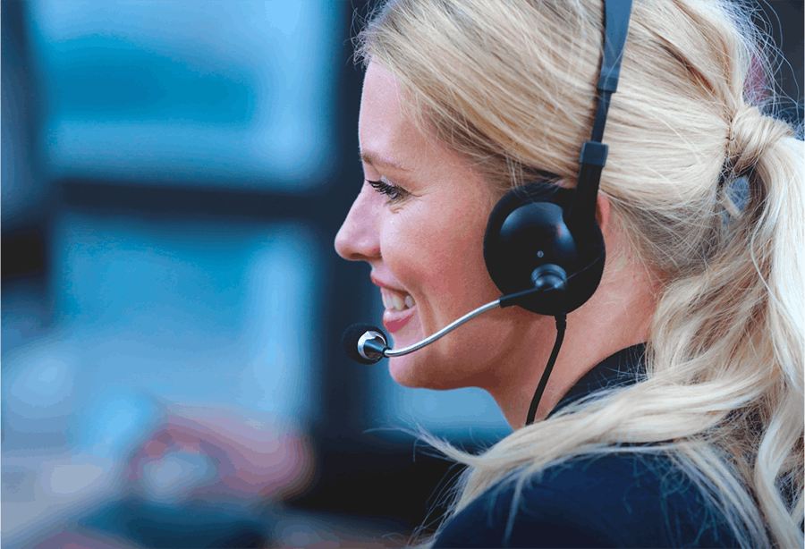 Blonde haired call centre woman wearing a black headset with blurred data screens in the background
