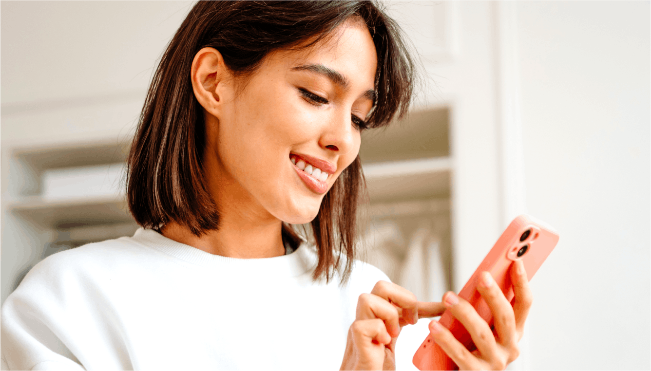 Smiling young woman with brown hair using her pink coloured phone
